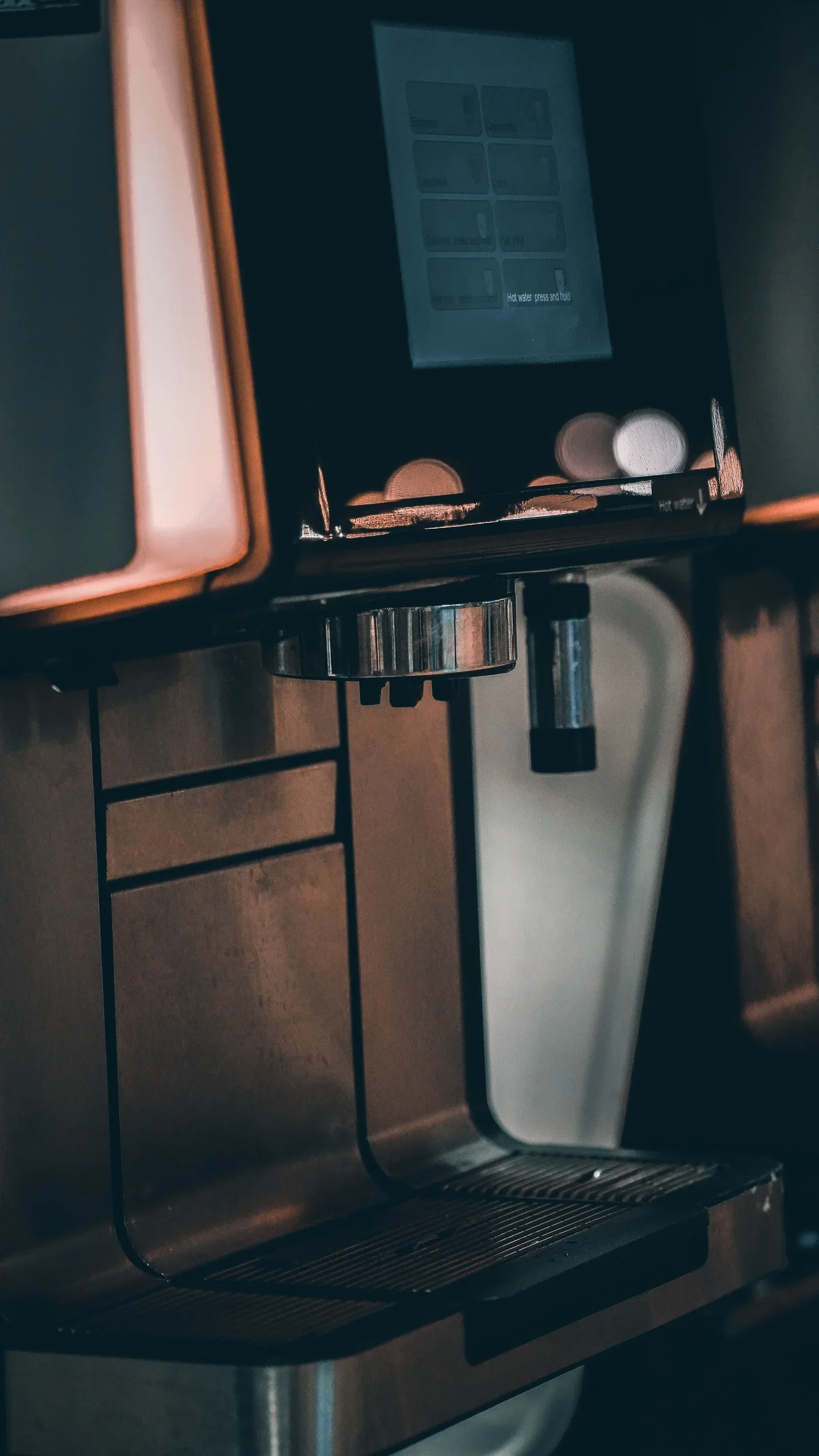 Close-up of an automatic coffee machine’s touchscreen, dispensing spouts and drip tray
